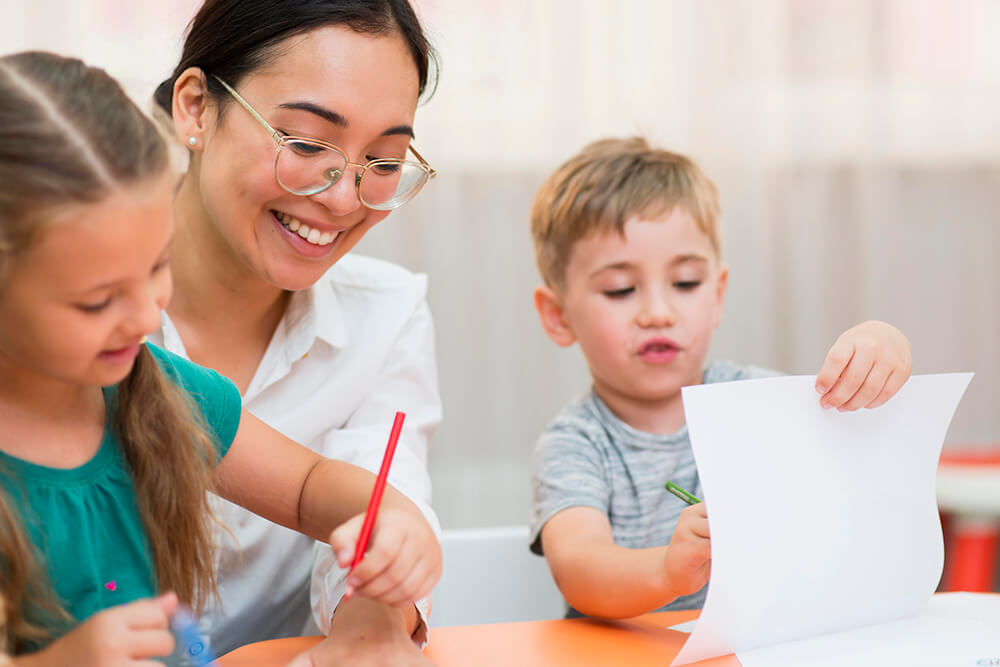 childcare teacher working with two kids with a pencil and a piece of paper